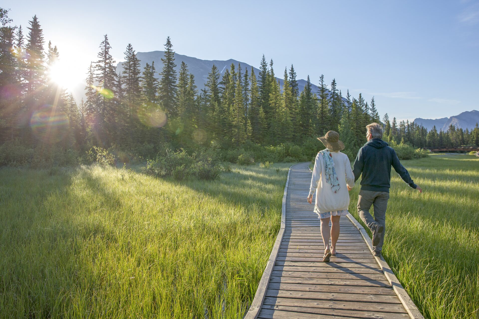 Retirement planning with Capital Wealth — a couple walks a sunlit boardwalk through a mountain meadow